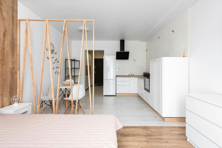 A compact studio apartment with smart Scandinavian interior design featuring a wooden room divider, white kitchen, and open-plan layout.