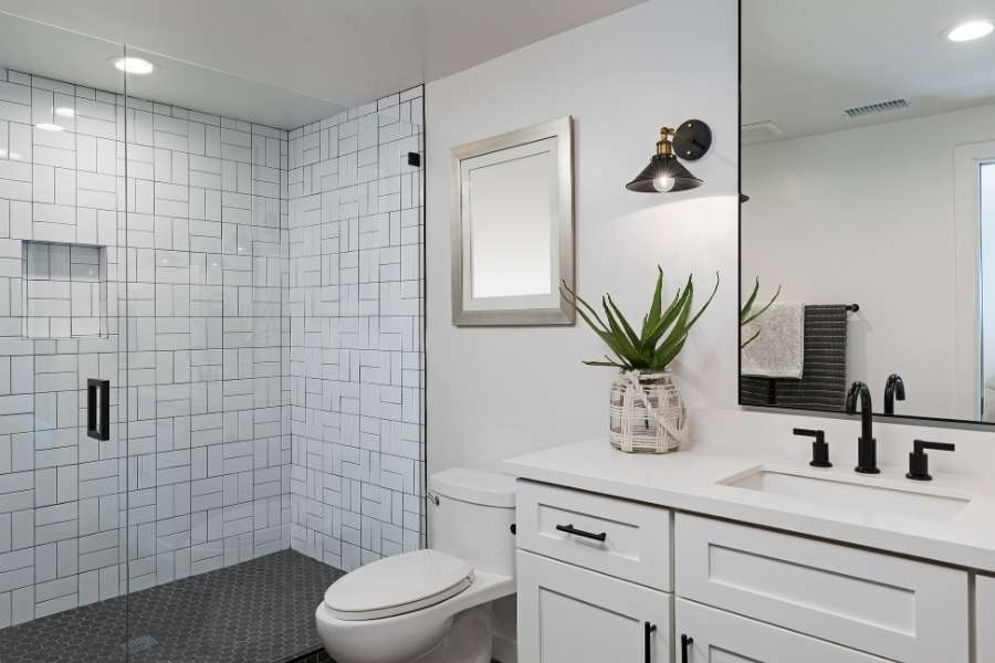 A modern bathroom storage vanity with white cabinets and black hardware next to a glass shower.