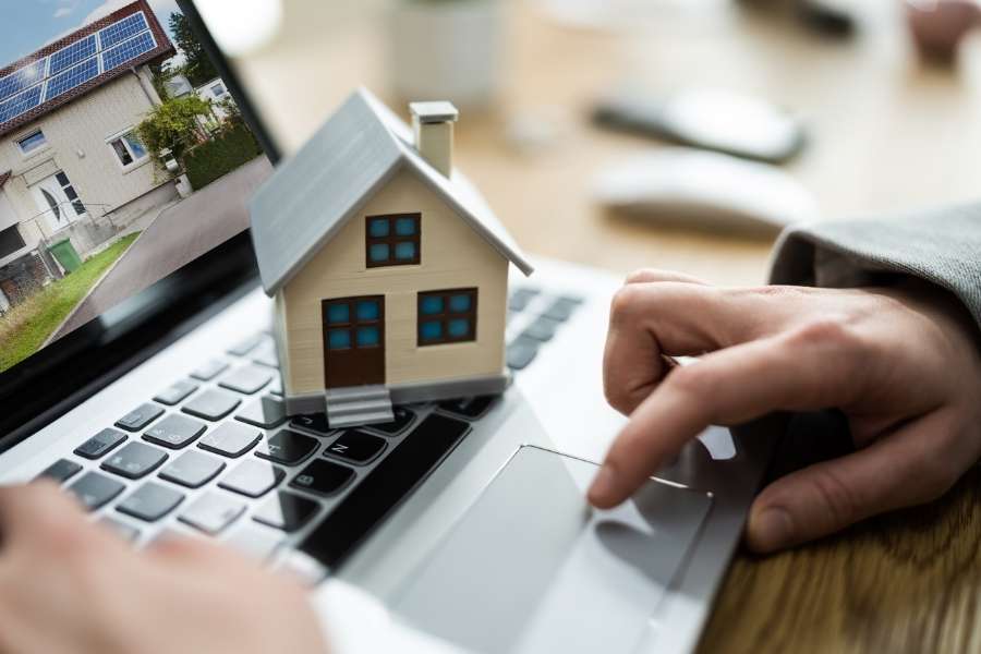 A person using a laptop with a model house placed on the keyboard to check hidden costs.