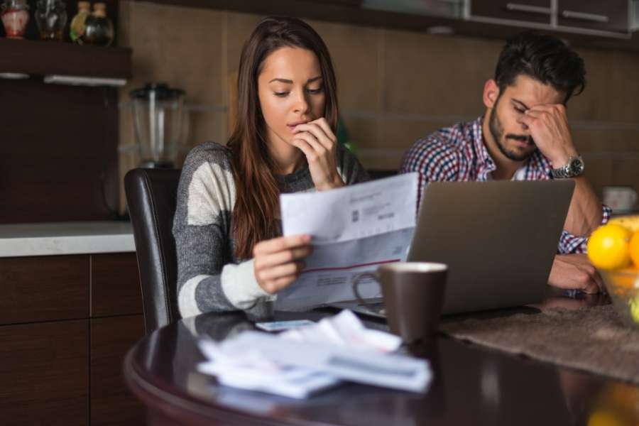 A concerned woman holding a utility bill while sitting next to a stressed man looking at a laptop.